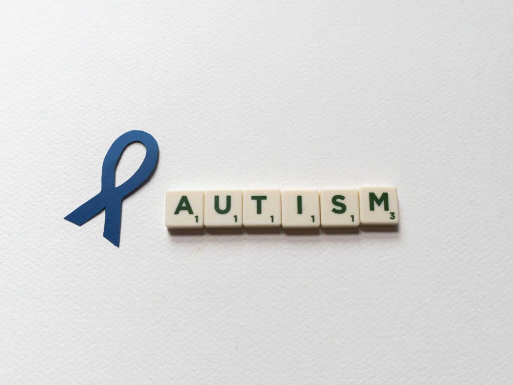 Blue ribbon and autism spelled with letter tiles symbolize autism awareness.